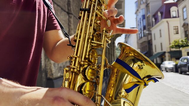 Male fingers of musician play the saxophone on summer day. Natural light reflects off metal surface, highlighting movement and rhythm. Scene captures live urban music and atmosphere street performance