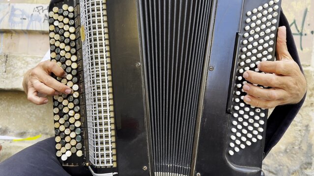 Male hands of musician playing the accordion at urban street. The detailed view highlights texture of instrument, capturing rhythm, tradition, and the expressive character of live music performance