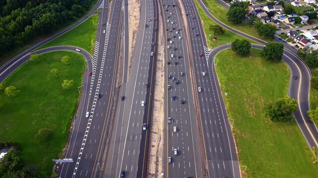Multi lane expressway and green grass median, New Jersey. Aerial view showing divided lanes, cloverleaf loop, moving vehicles and suburban fringe.