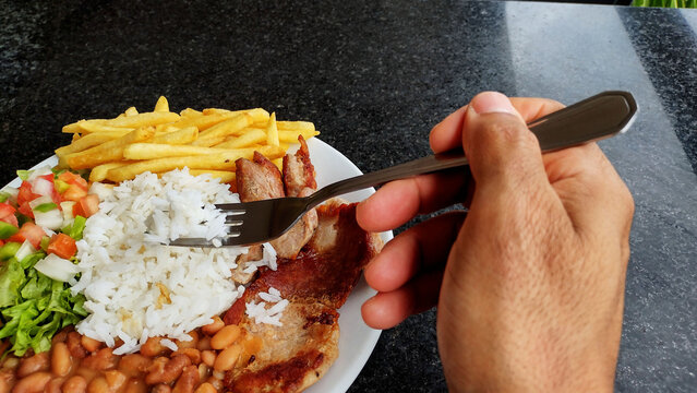 Person eating a hearty meal of rice beans french fries meat and salad with a fork