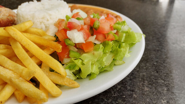 Delicious plate of rice beans french fries and fresh salad with tomatoes and lettuce