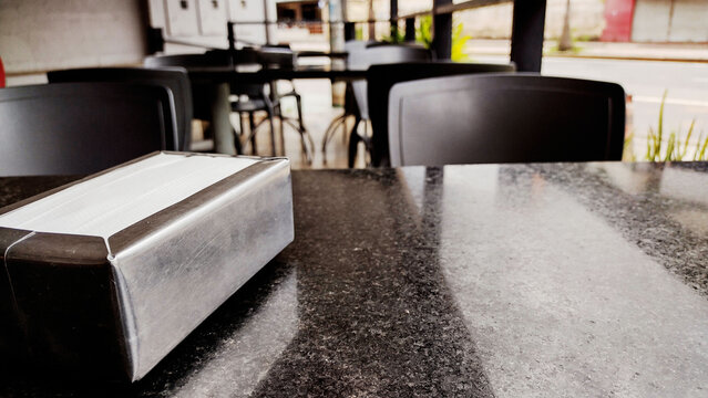 Close up of a stainless steel napkin holder on a granite table in a restaurant with blurred background