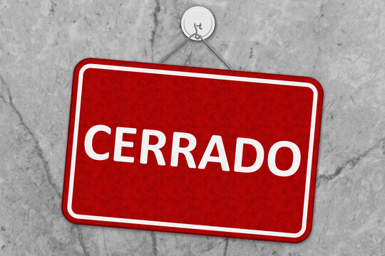 Closed red and white sign Cerrado in Spanish on grey stone