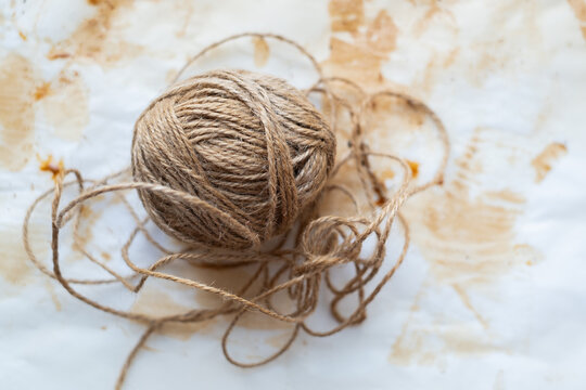 Ball of natural jute twine with loose tangled strings on white parchment paper with brown stains, rustic craft and eco packaging material