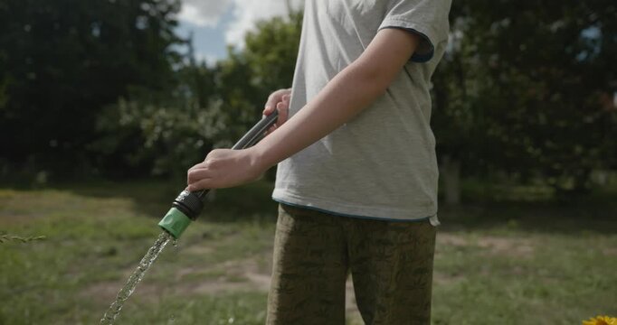 Close-up children hands watering plants in backyard. 4K 10-bit