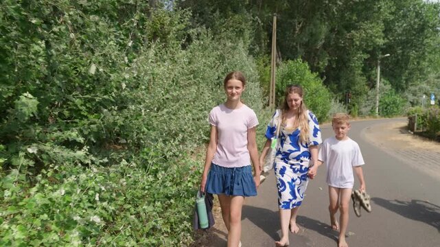 Woman and two children walking along a tree lined road a family walk barefoot