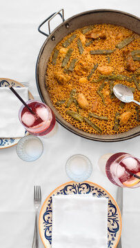 Traditional Spanish Valencian paella with chicken and beans, served in a pan on a restaurant table next to refreshing glasses of tinto de verano. Authentic Mediterranean gastronomy concept