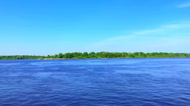 Calm view at the Volga river and the Borsky District in Nizhny Novgorod Oblast, deep blue rippling waters and a stretch of land strewn with green thickets on the horizon, under a mostly clear sky