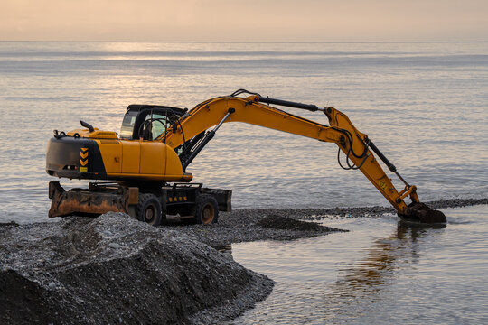 Heavy excavator deepens coastal river channel and removes mud, gravel and stones deposited after prolonged rain. Maintenance reduces blockage and restores water flow through river mouth into sea.