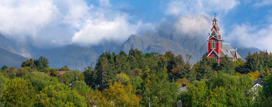 Red church in Klokkarvika surrounded by autumn forest and dramatic mountains in the Lofoten Islands
