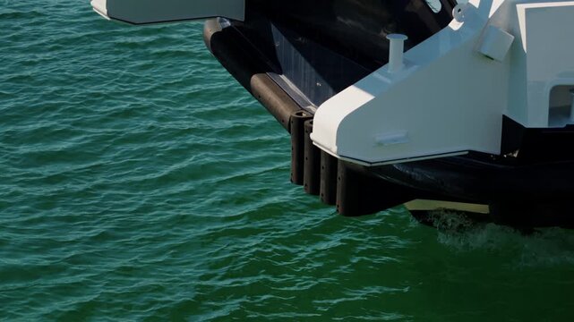 Close-up of a ferry bow corner with white bollards and black rubber fenders over green sea water, French Riviera, France.