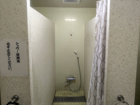 シャワーカーテンのある個室シャワーと止水の注意書き 屋内プールのシャワーブース