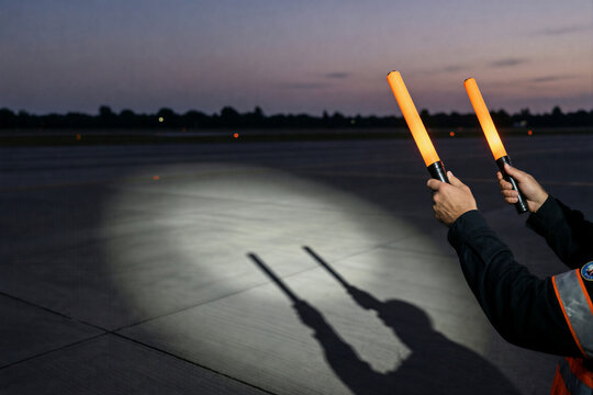 Airport marshal holding illuminated orange batons at night