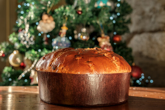 Panettone Christmas cake displayed on a wooden table beside a glowing decorated tree