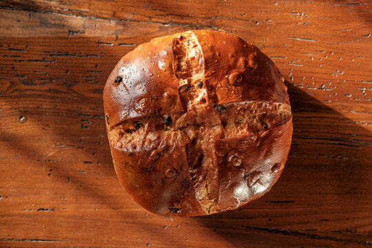 Bread loaf with raisins and cross score on a rustic wooden table