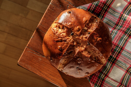 Panettone bread with raisins and cross cut on a rustic table in warm sunlight
