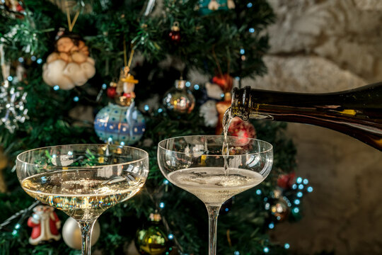 Champagne pours into coupe glasses beside a glowing Christmas tree for holiday celebration