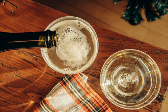 Champagne pours into coupe glasses on a rustic table with evergreen branches and warm holiday light