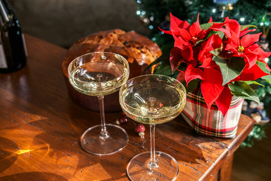 Champagne glasses and panettone set a festive Christmas table with poinsettia and glowing tree lights