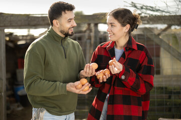 Portrait of happy farmers holding chicken eggs near chicken coop on farm © JackF