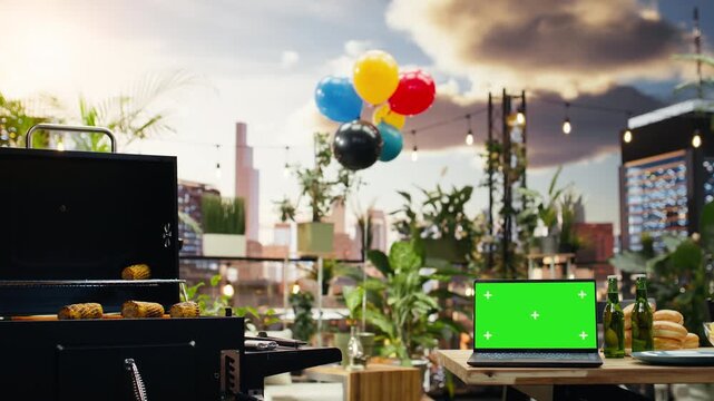 Green screen laptop mockup sits on a rooftop barbecue table beside drinks, bread and tableware, offering an editable display for outdoor event advertising.