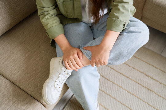 Ankle pain and injury, woman holding her sore leg with discomfort while sitting on a sofa at home during recovery from a physical strain or accident