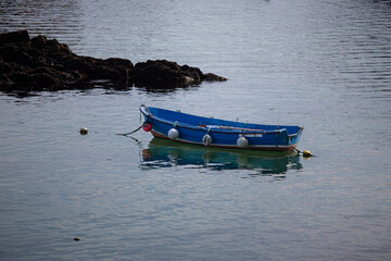 Blue wooden rowing boat moored with colorful buoys on calm sea water near rocky coast © NaturePix