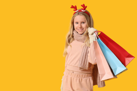 Holiday shopping and winter sales, happy girl with reindeer antlers headband holding colorful paper bags on a bright yellow background
