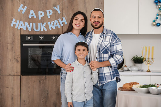 Hanukkah celebration, happy family with son standing in kitchen at home during Jewish holiday, festive home decor and traditional menorah on table