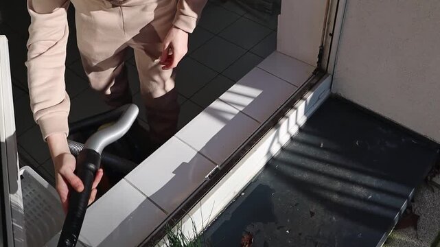 Young Caucasian guy in hoodie standing in kitchen and vacuuming trash from bottom inside window frames preparing to wash window on sunny day, close up top side view with slow motion. Window frame repa