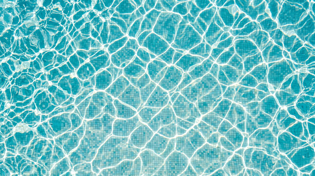 High angle view of bright sunlight caustics rippling on the surface of a turquoise swimming pool with blue mosaic tiles on the bottom creating a beautiful wavy light pattern.