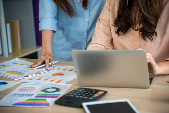 Two businesswomen talking together at office desk got happiness good news. Two start up business partners enjoy good news from smartphone. Success confident women teamwork. Asian woman Business