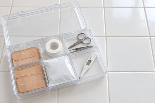 Open clear plastic first aid organizer box with adhesive bandages, medical tape, scissors, tweezers, cold pack and thermometer