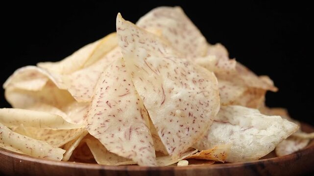 A pile of crispy fried taro chips slowly rotating against a black background.