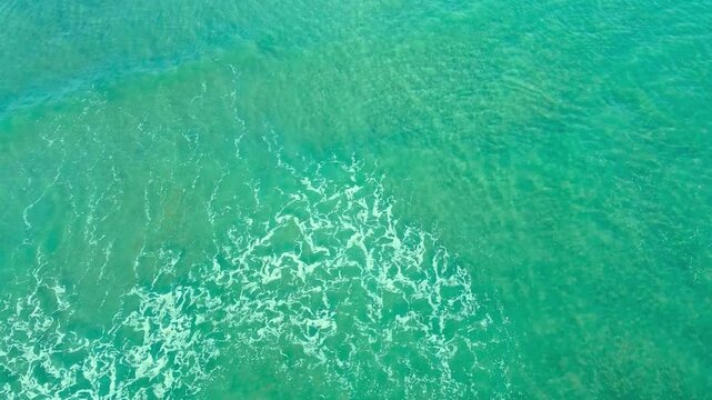 Aerial view of turquoise ocean waves crashing on sandy beach surface