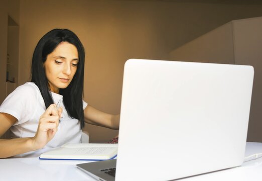 Young long dark haired georgian woman takes notes in her living room. Laptop lid screen blank space background. Tbilisi