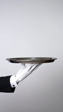 A gloved hand holds an empty silver platter against a plain background