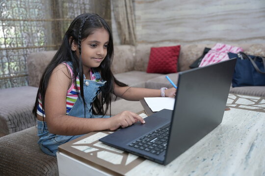 Cute little Indian girl child studying on laptop while sitting on sofa at home