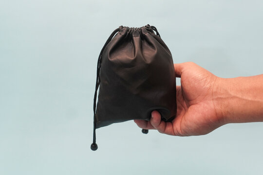 Hand holding small black drawstring pouch against a plain light blue