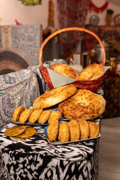 Traditional Kazakh pastries and freshly baked bread arranged on a table with ethnic ornaments. Golden homemade baursaks, savory pastries and round flatbreads served in a traditional Central Asian sett