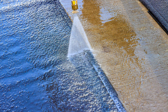 Air pressure washer directs water over car carpet outdoors, with wet dry areas visible.