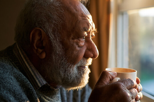Elderly man holding a hot cup near a window during golden hour