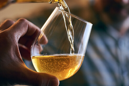 Amber liquid pouring into a modern glass held by a person with golden cold drink