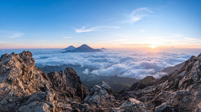 Breathtaking sunrise view above clouds from a rocky mountain peak with distant volcanoes on the horizon