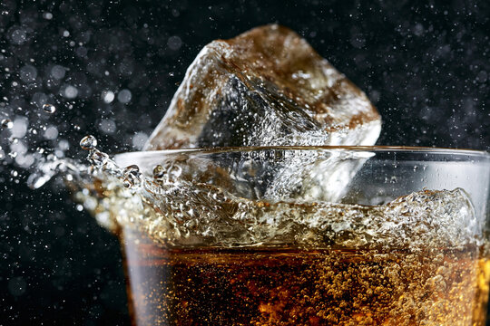 Ice cubes dropping into a glass of dark liquid creating big splashes with cold drink