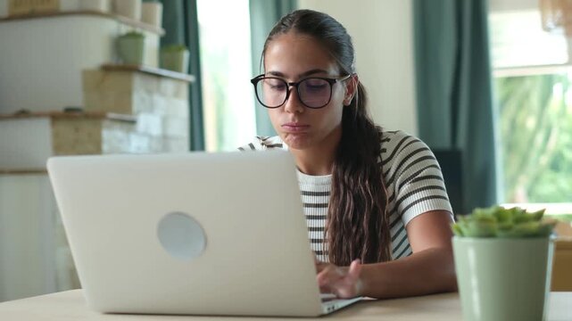 Overworked young freelancer with glasses suffering from a headache and eyestrain while working long hours on her laptop, feeling tired and massaging her temples from the pressure and stress