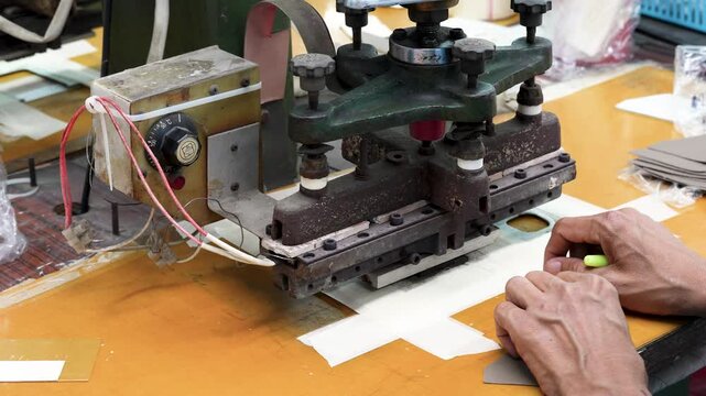 Worker embossing and debossing logo on genuine leather piece using industrial heat press stamping machine in workshop.