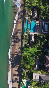 Straight down vertical drone shot of luxury tropical resort with turquoise pools, green lawns, and palm tree shadows on sandy beach. Great for social media reels.Semenyak beach. Bali.