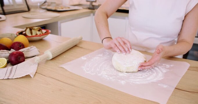 Pastry making. Home cooking. Female baker hand flattering flour dough piece on paper parchment sheet preparing for baking in kitchen.