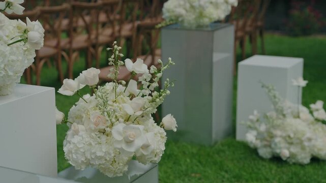 Aisle decor at an outdoor ceremony in Portugal, with roses, hydrangeas and stock in low arrangements on white boxes next to rows of guest seats.